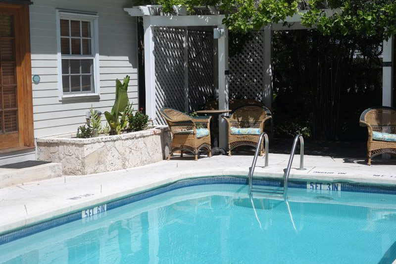 Pool with stone coping, pergola, and tropical seating