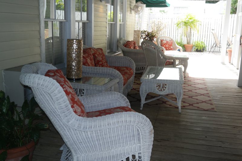 Covered veranda with white wicker furniture and coral cushions