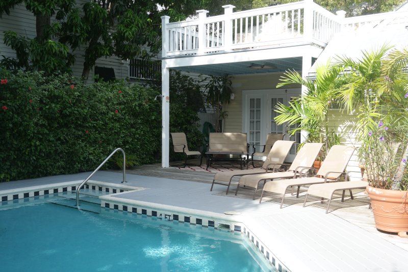Pool deck with lounge chairs, upper balcony, and tropical plantings