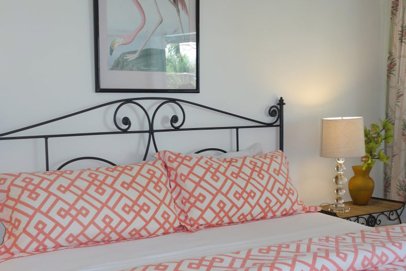 Bed headboard detail with wrought-iron scrollwork and coral and white bedding