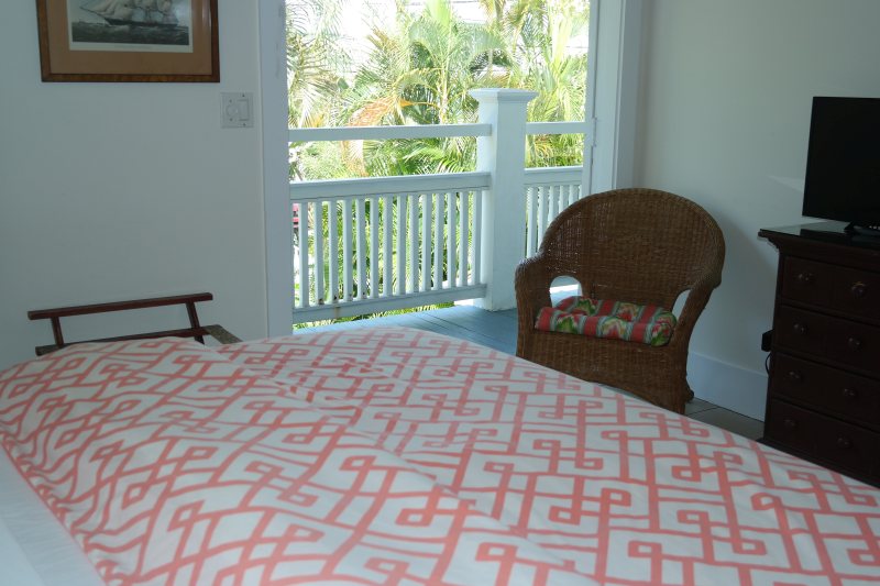 Room with open balcony door showing palm canopy and wicker armchair