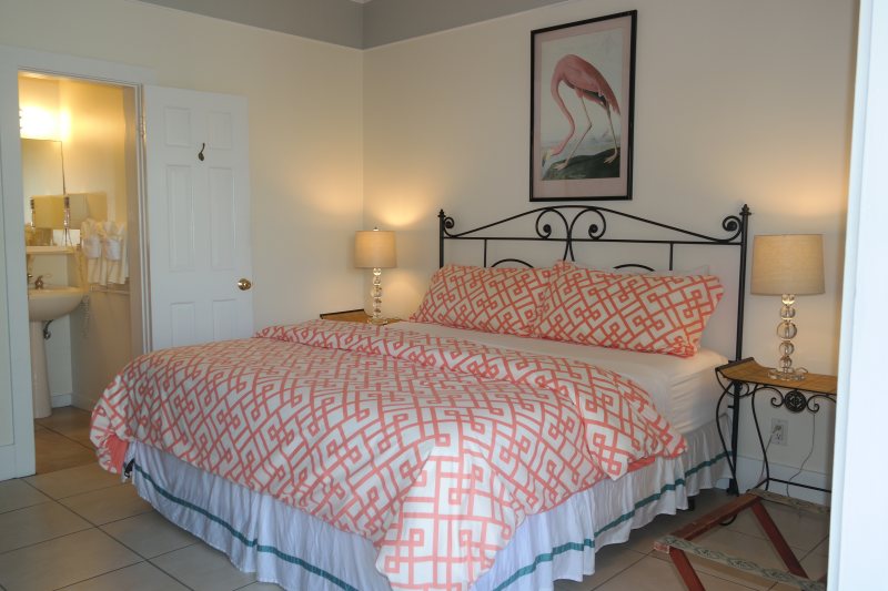 King room with flamingo art, coral bedding, and en-suite bathroom glimpse