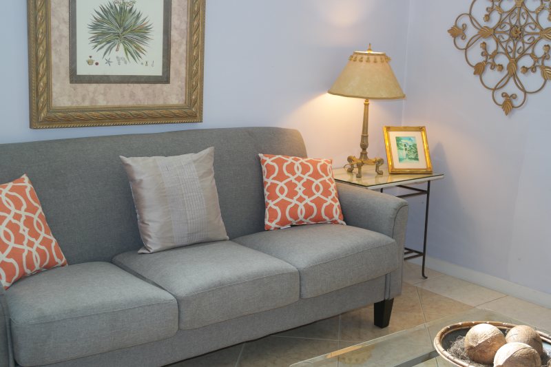 Suite sitting room with grey sofa, coral accent pillows, and botanical art